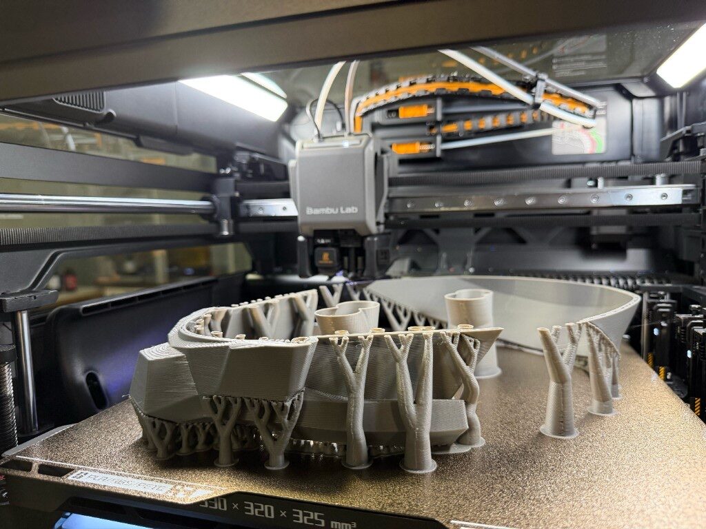 Bambu Lab filament printer mid-print with tree supports and parts on the build plate