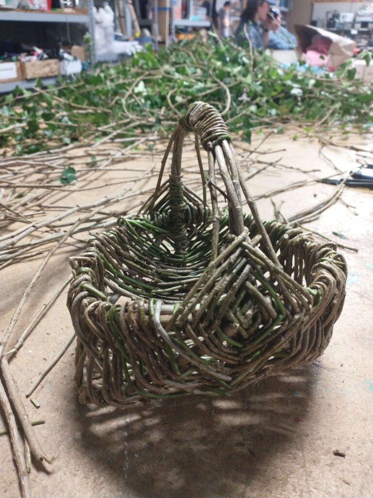 Handwoven twig basket with green vines and branches on a workshop table