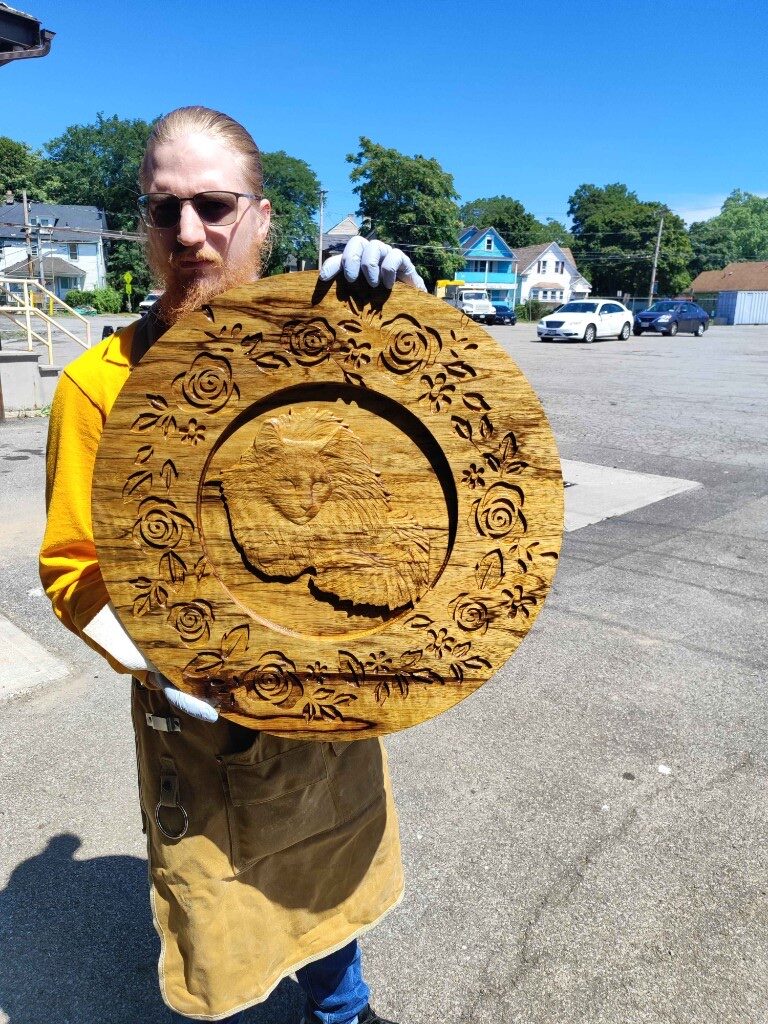 Maker holding a round CNC-carved wooden plaque with a cat relief and rose border