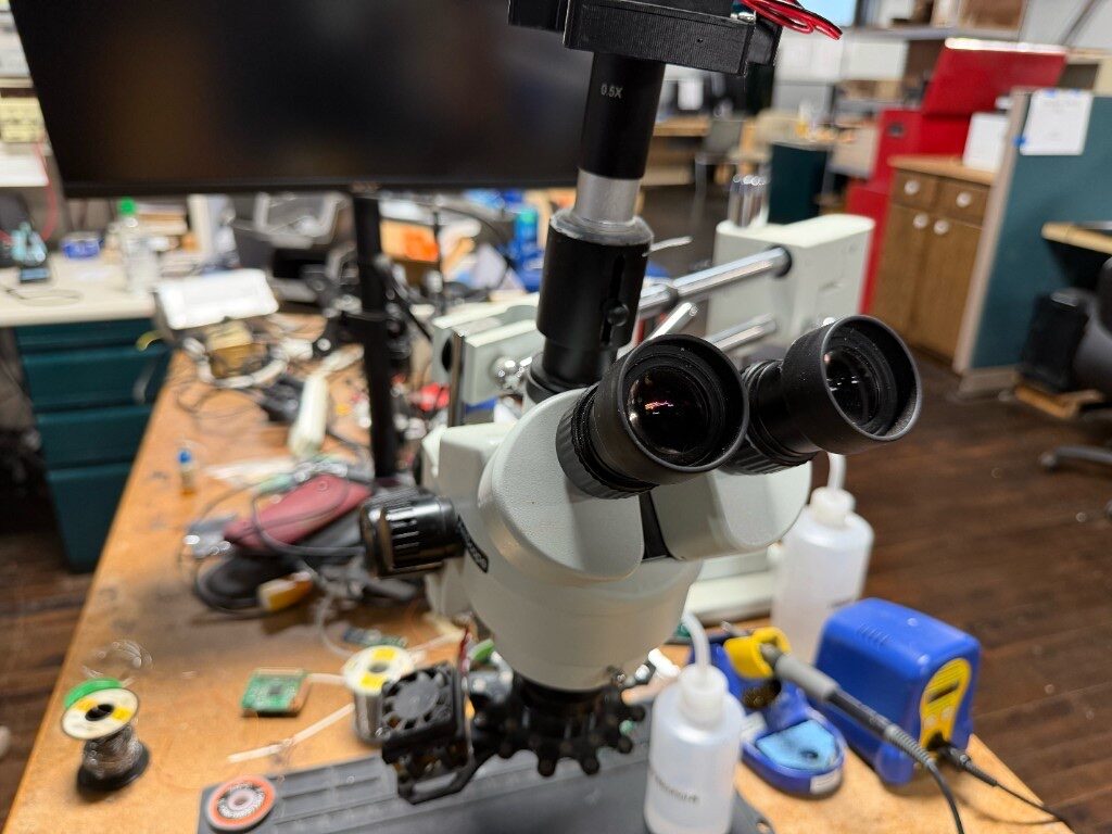 Stereo microscope and blue soldering station on a wood electronics workbench