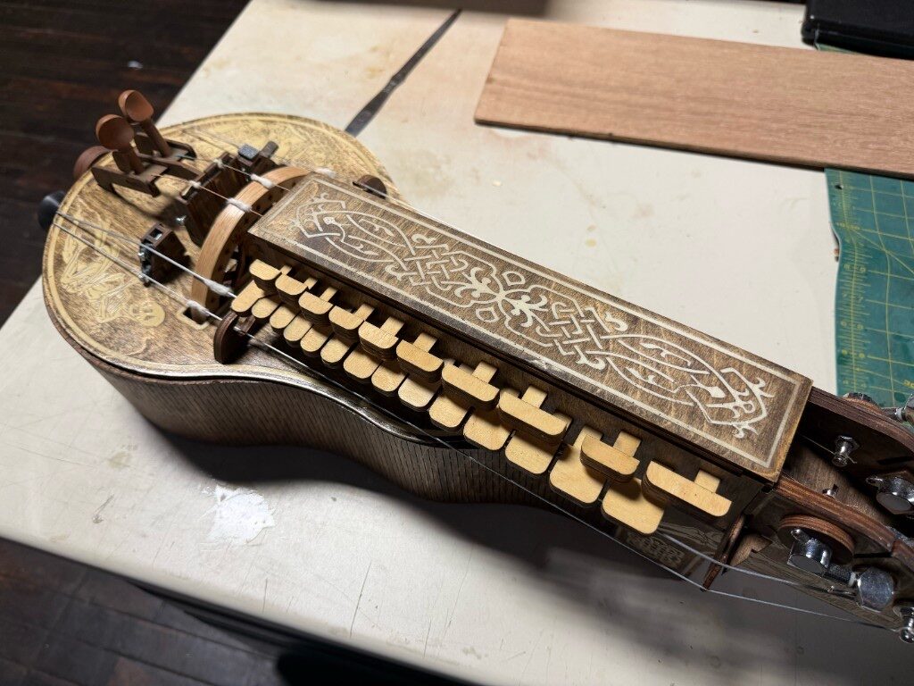 Wooden hurdy-gurdy with intricate laser-engraved Celtic knotwork on the keybox