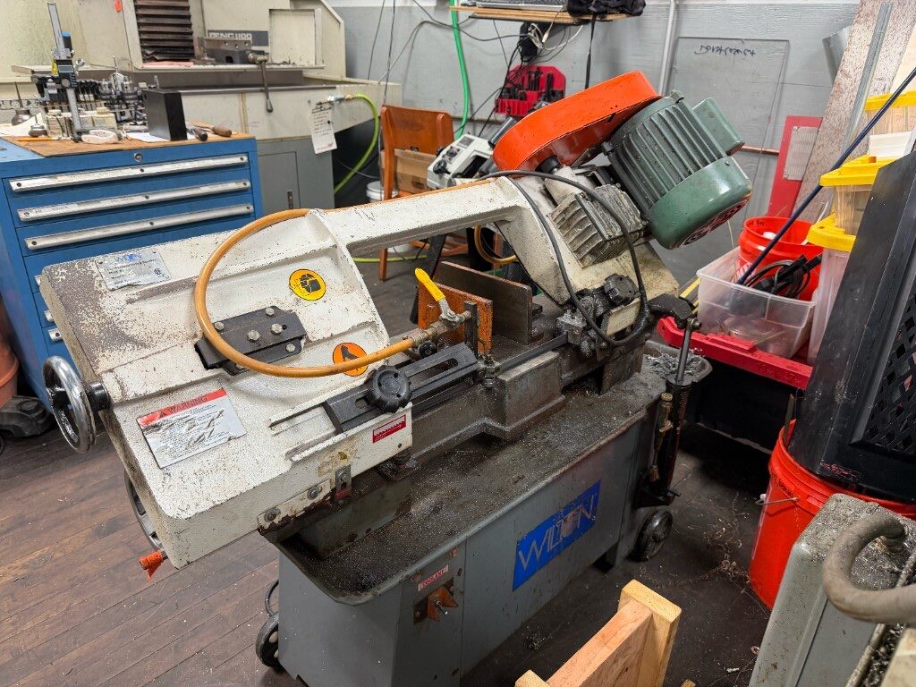 Wilton horizontal band saw with coolant hose and orange motor guard in the machine shop