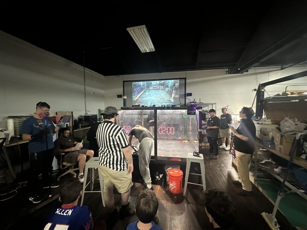 Robotics competition arena with a referee, makers, and a projected live feed of the match
