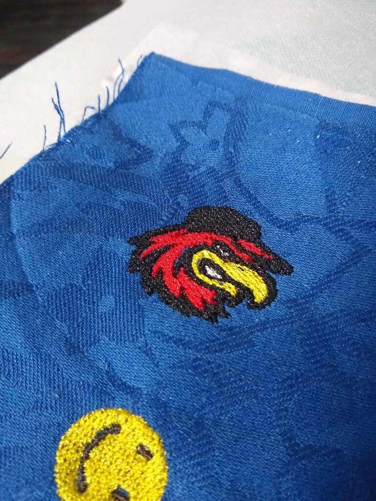 Close-up of embroidered mascot and smiley designs on blue patterned fabric