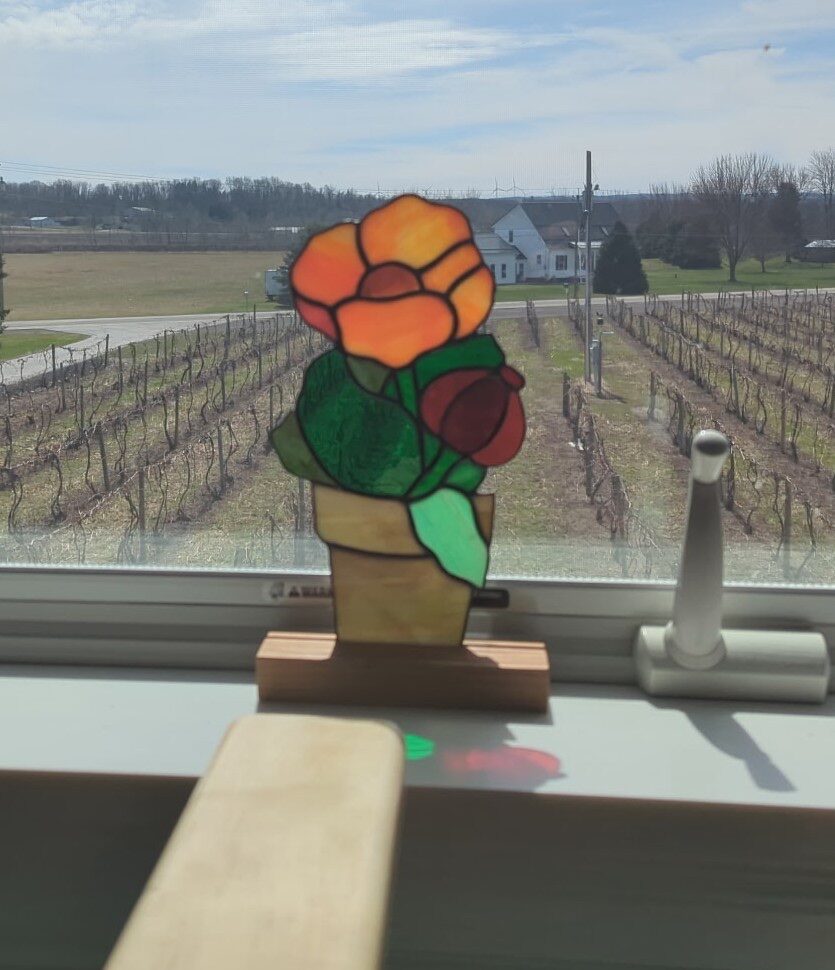 Stained glass potted flower in a wood stand on a sunny windowsill