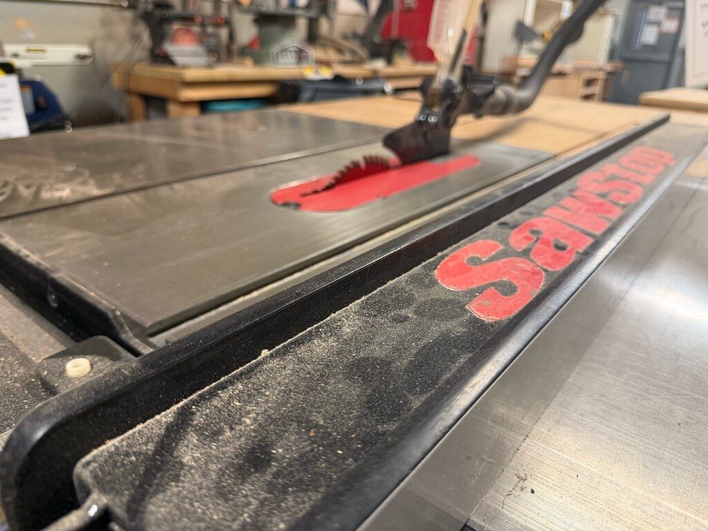 SawStop table saw fence and blade with dust collection hose in the wood shop