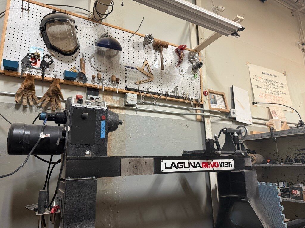 Laguna Revo wood lathe in front of a pegboard with face shields and tools